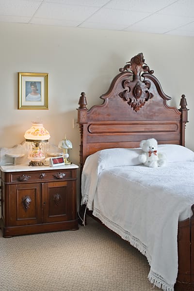 A vintage bedroom featuring an antique wooden headboard and a classic nightstand with a decorative lamp.