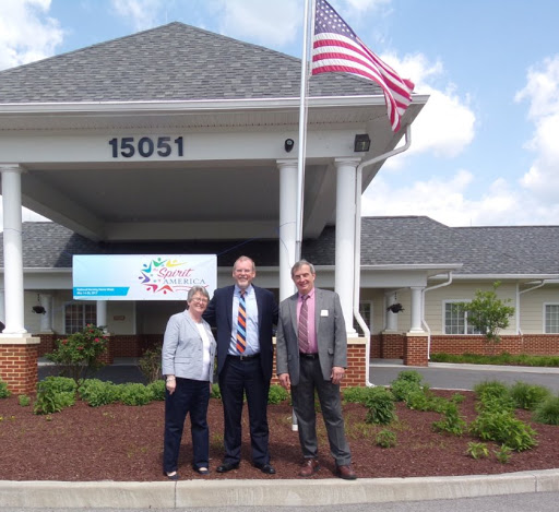 A group of three people standing in front of a building with an American flag.