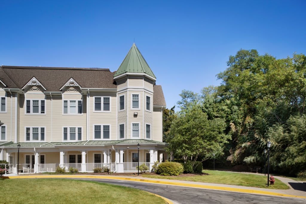 A Victorian-style house with a distinctive tower, surrounded by trees on a sunny day.