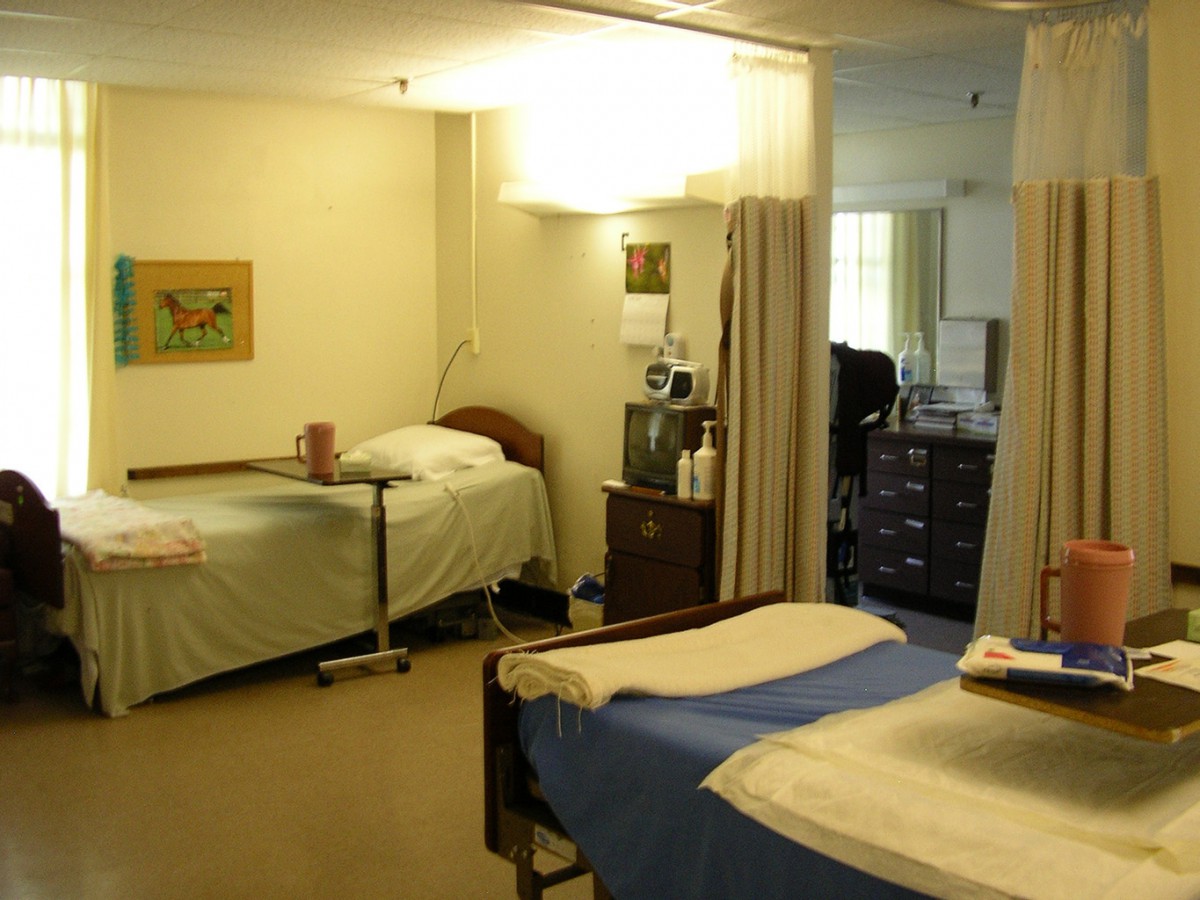 A hospital room with two beds separated by a curtain, featuring medical equipment and supplies.