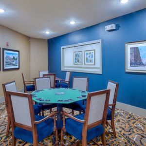 A cozy poker room featuring a card table surrounded by chairs, adorned with wall art on a blue accent wall.