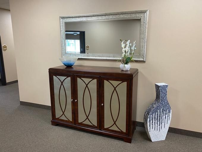 An elegant entryway setup featuring a wooden cabinet with decorative doors, a large wall mirror, and vases for added style.