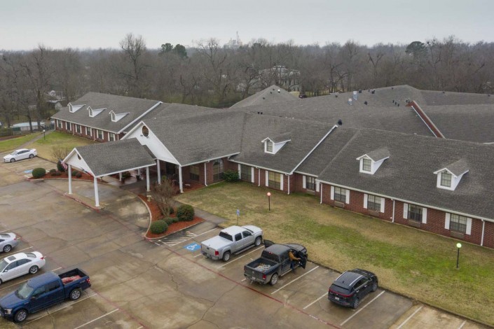 Aerial view of a large residential building with a parking lot and several cars on an overcast day.