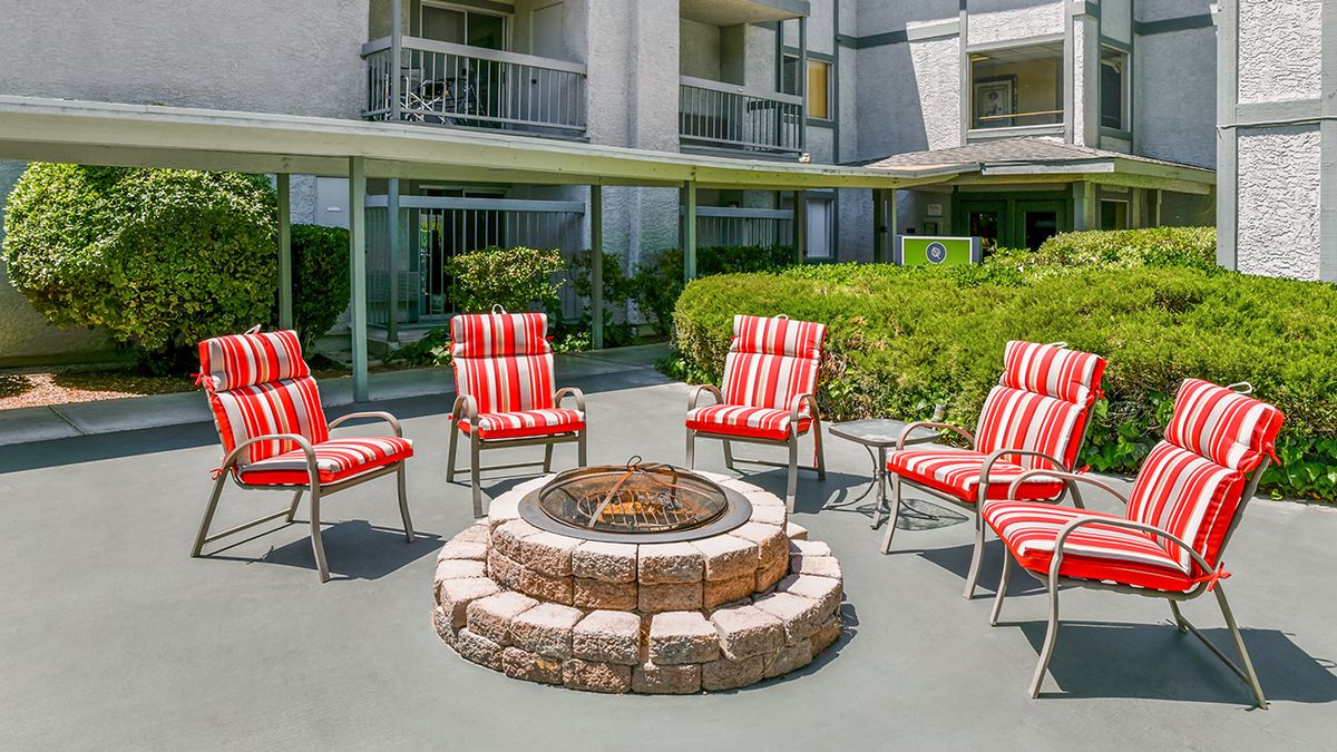 An outdoor patio area with a fire pit surrounded by red and white striped chairs at an apartment complex.