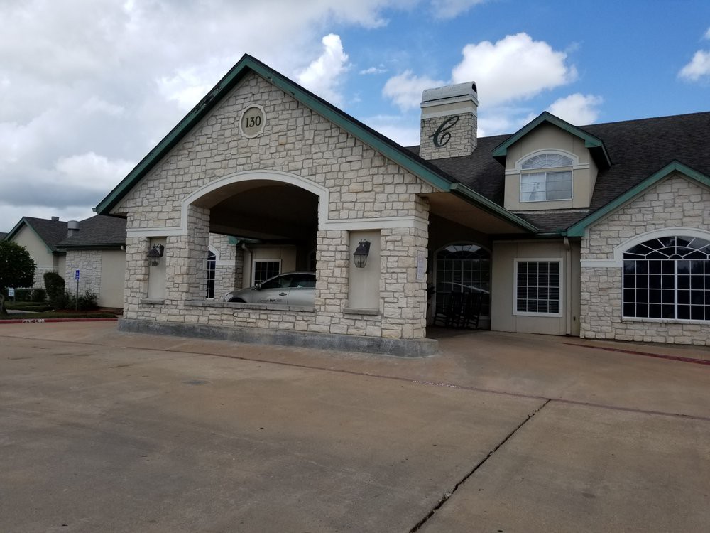 A stone exterior building with a covered entrance and driveway under a cloudy sky.