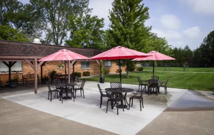 Outdoor patio area with tables, chairs, and red umbrellas surrounded by a green lawn.
