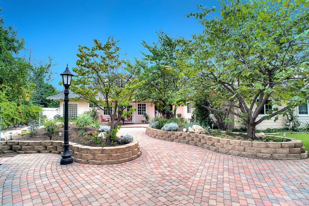A charming house surrounded by a lush garden with a brick pathway and lamp post.