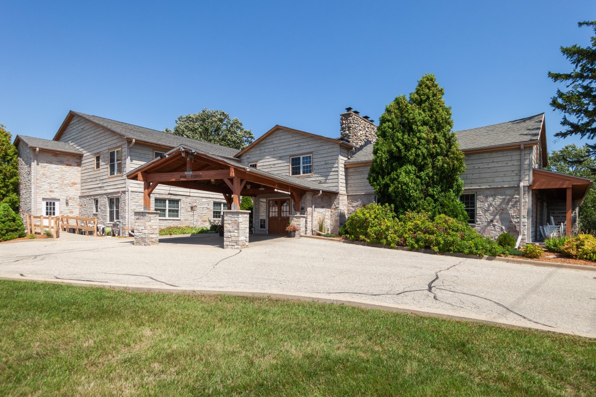 A spacious residential home with a stone exterior and a covered driveway, surrounded by lush greenery.