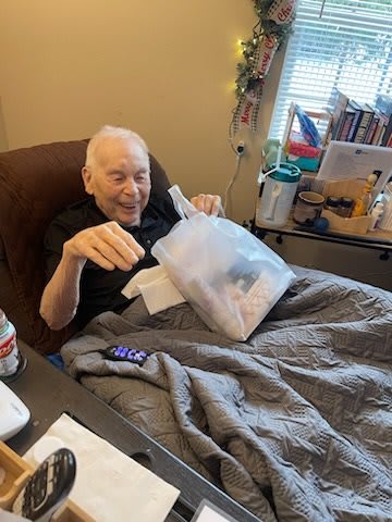 An elderly man sits in bed, smiling while reading a document.