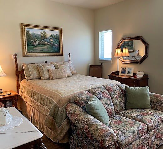 A cozy bedroom with a bed, floral sofa, decorative lamp, and artwork on the wall.