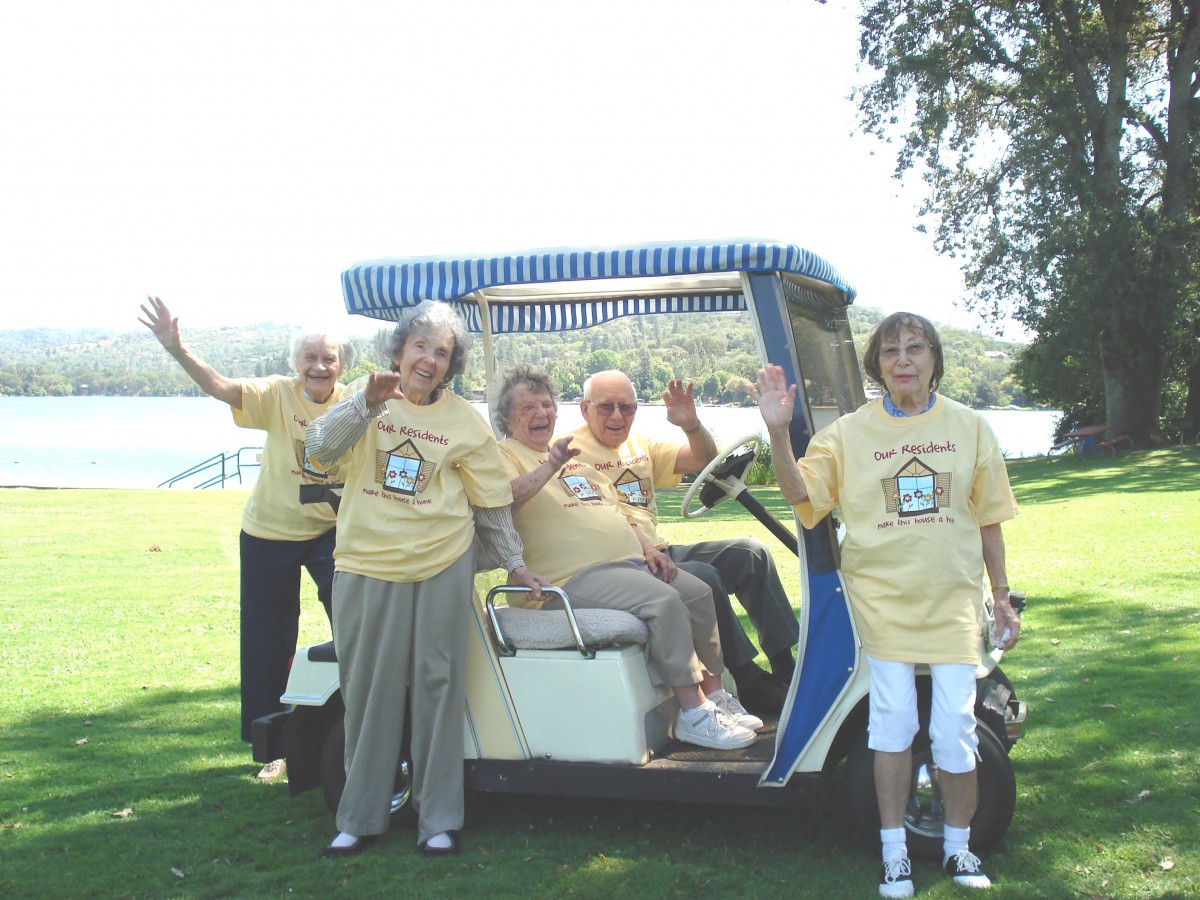 A group of people enjoying a day outdoors, gathered around a golf cart and waving.