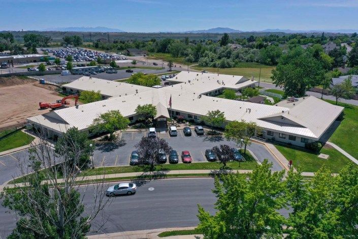 Aerial view of a building with a parking lot surrounded by trees and a road.
