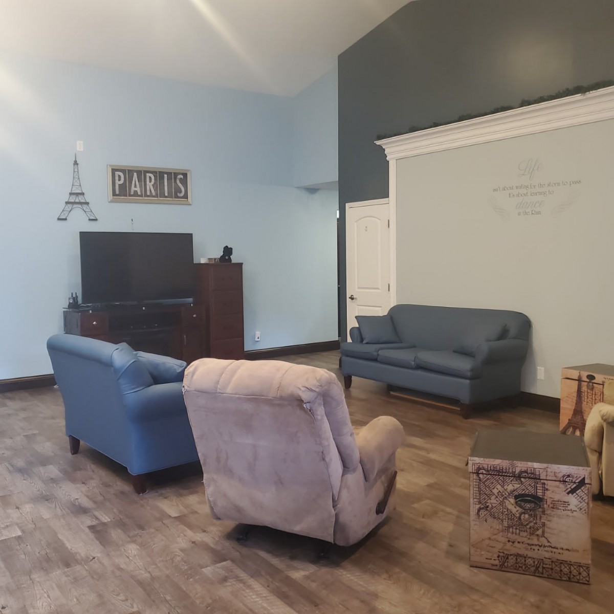 A cozy living room with sofas, armchairs, and a TV set against a wooden floor.