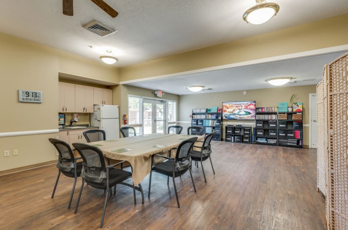 A spacious community room with tables, chairs, and a kitchen area, suitable for meetings and gatherings.