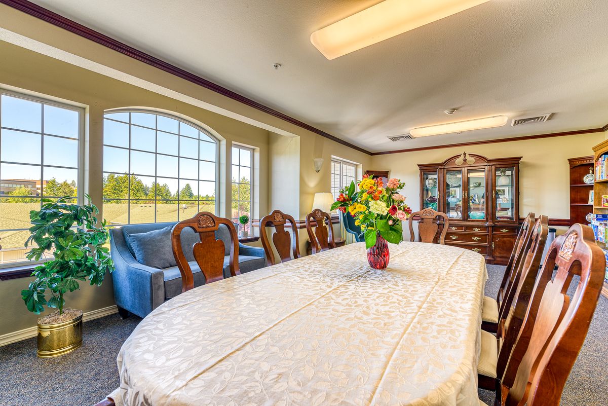 A spacious and elegant dining room with a large table, adorned with a floral centerpiece, surrounded by classic wooden chairs.