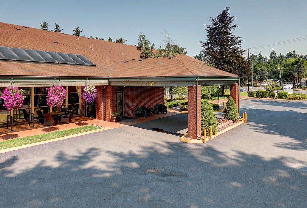 A building entrance with hanging flower baskets and a driveway surrounded by trees.