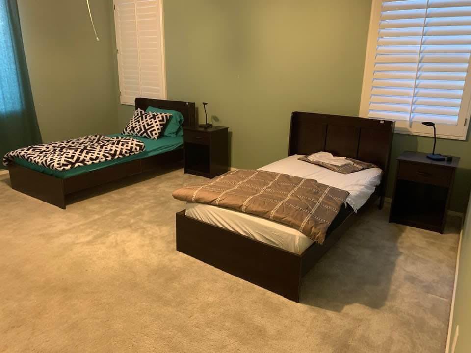 A bedroom featuring two single beds with nightstands, carpeted floors, and a window.