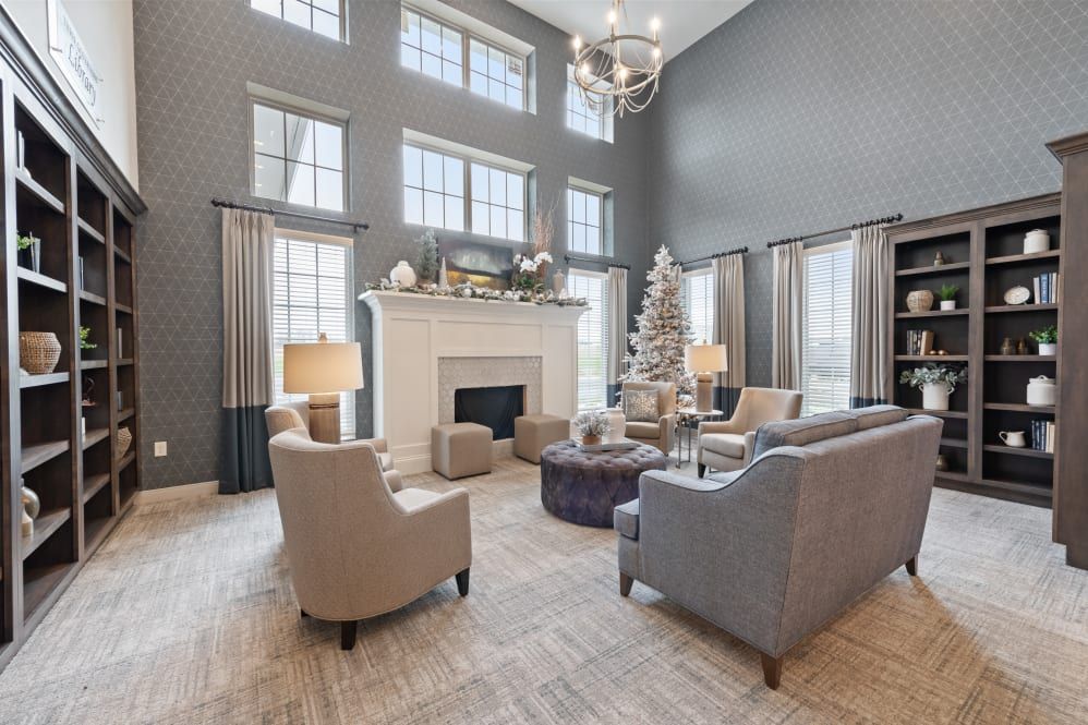 A spacious and elegant living room featuring high ceilings, large windows, and a beautifully decorated Christmas tree beside a white fireplace. The modern furniture and neutral color palette create a warm and inviting atmosphere.