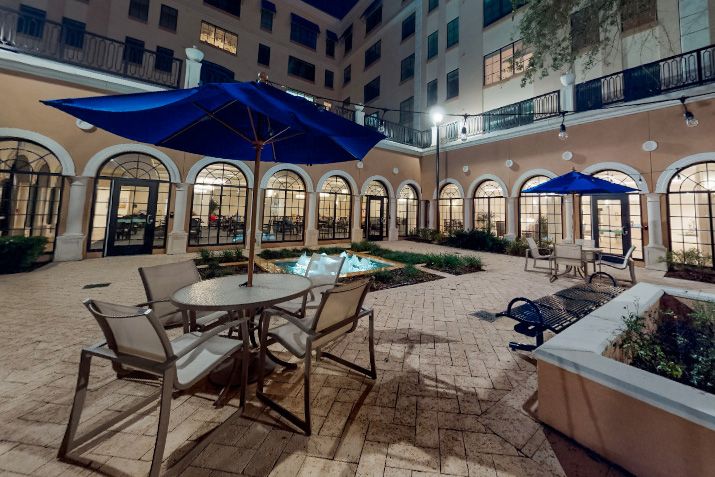 A nighttime view of a courtyard with patio furniture and umbrellas, surrounded by an arched building.