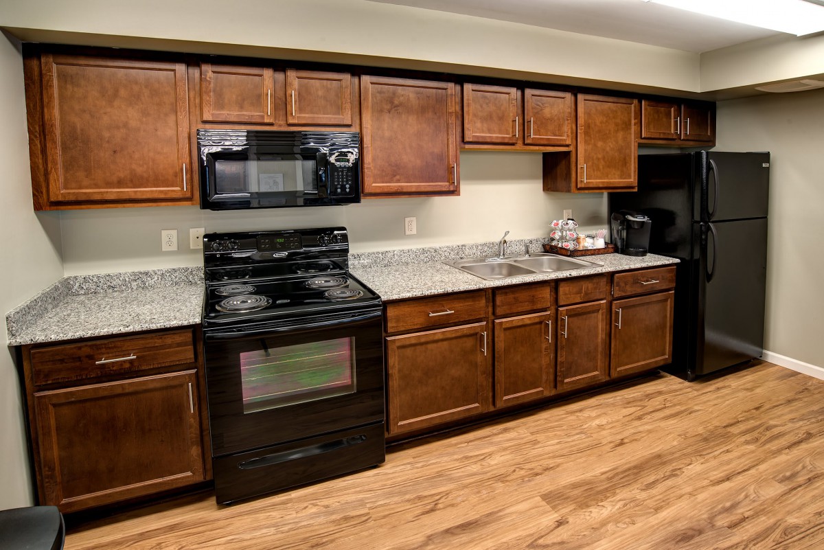 A modern kitchen with wooden cabinets, black appliances, and wood flooring.