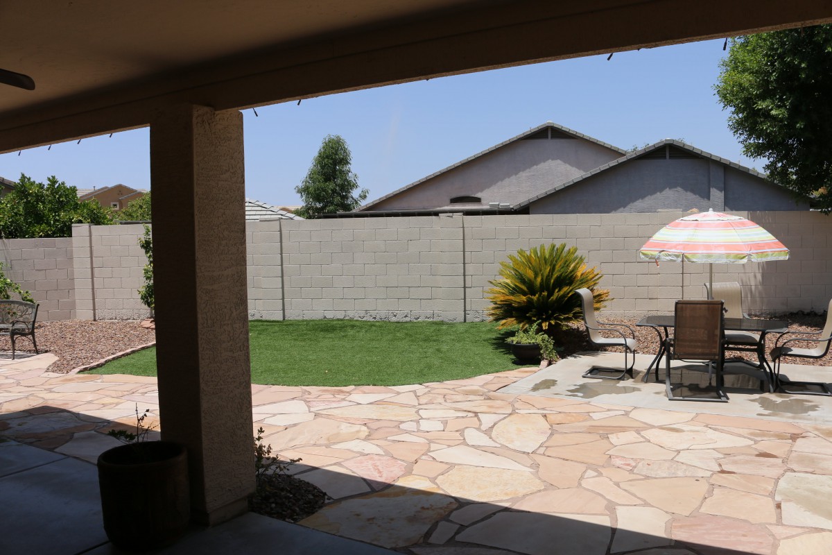 A sunny backyard with a patio area, featuring outdoor furniture and an umbrella.