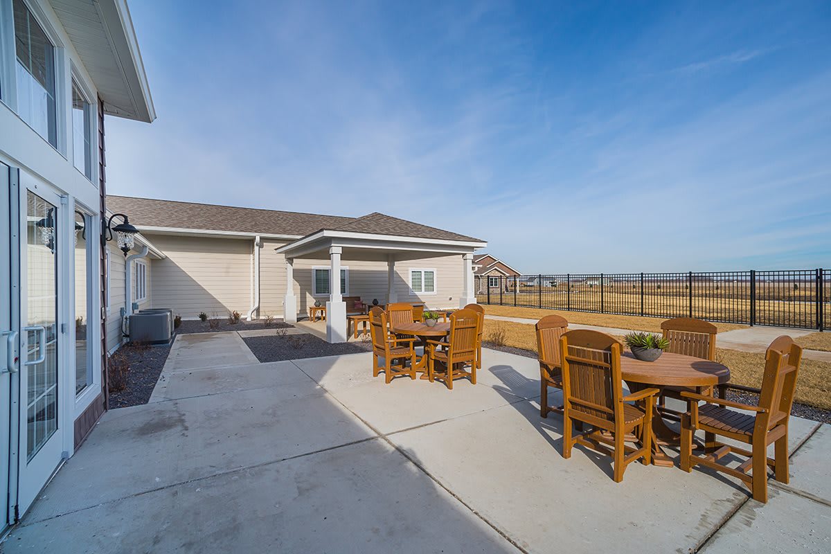 A spacious backyard patio with wooden tables and chairs under a clear blue sky.