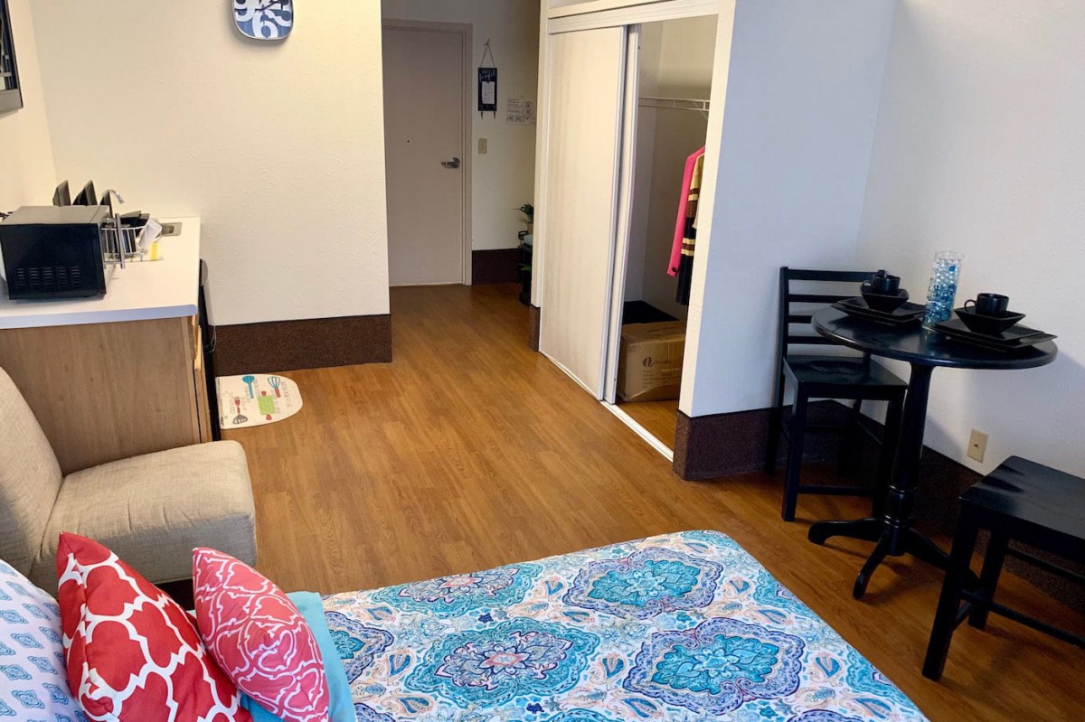 A cozy bedroom with a bed, desk, and closet featuring wooden flooring.