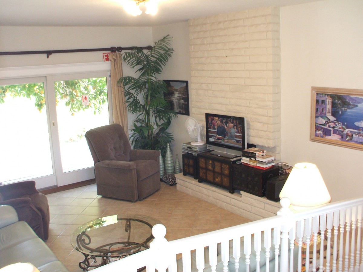 A cozy living room featuring a recliner, television, and coffee table next to a brick accent wall and sliding glass door.