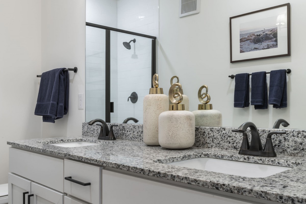 A modern bathroom with a granite countertop, double sinks, and decorative jars.