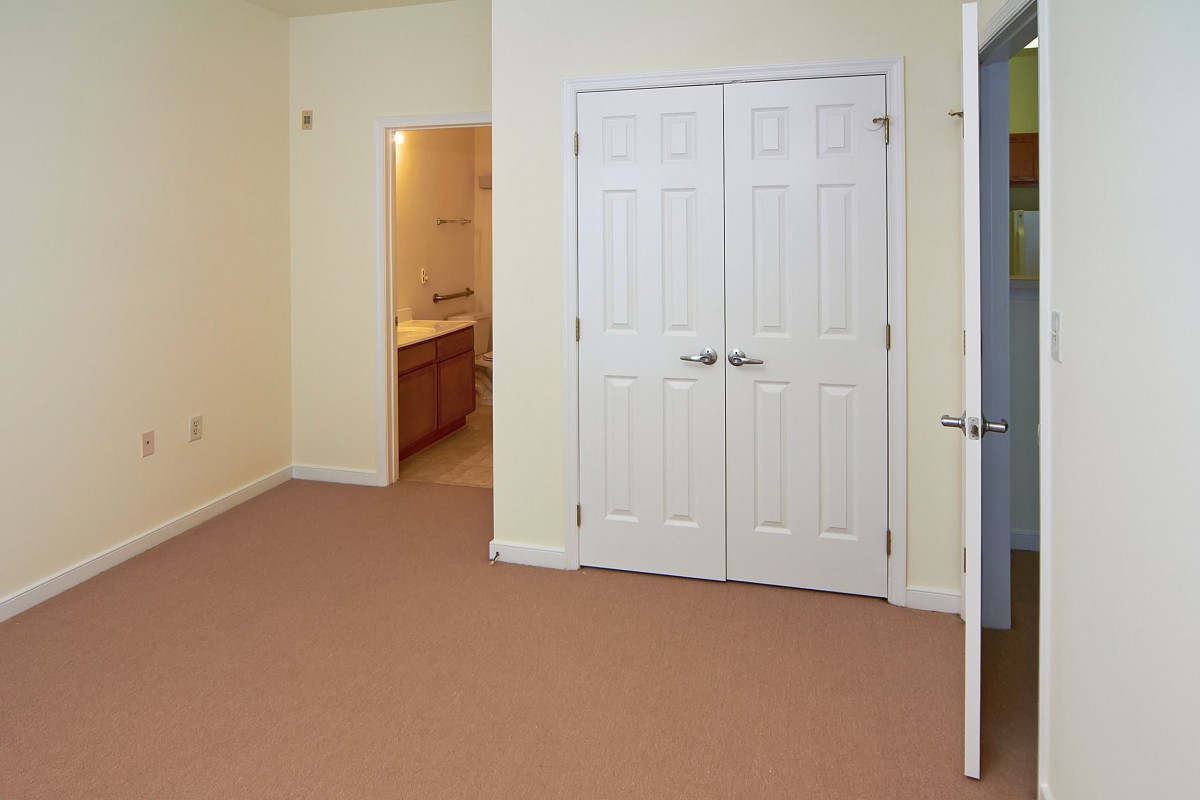 An empty bedroom featuring a double-door closet with beige carpeting.