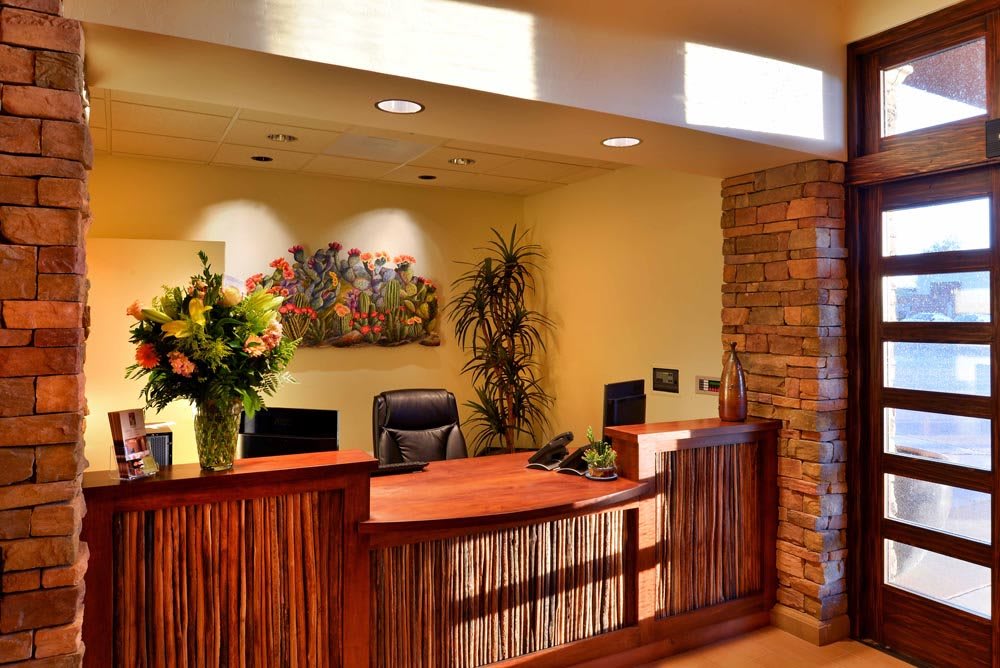 A warm and inviting reception area featuring a wooden desk, decorative plants, and artwork.
