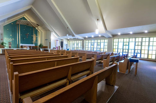 Interior view of a church featuring wooden pews and large windows.
