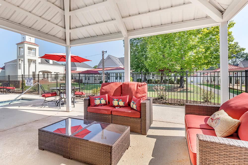 A cozy outdoor seating area under a gazebo with red cushioned furniture by the pool.