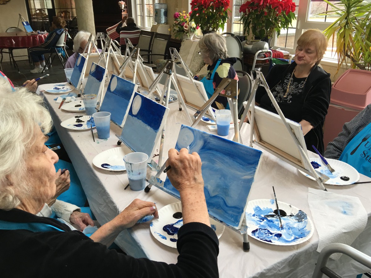 A group of seniors participating in a painting class, each working on their own canvas.