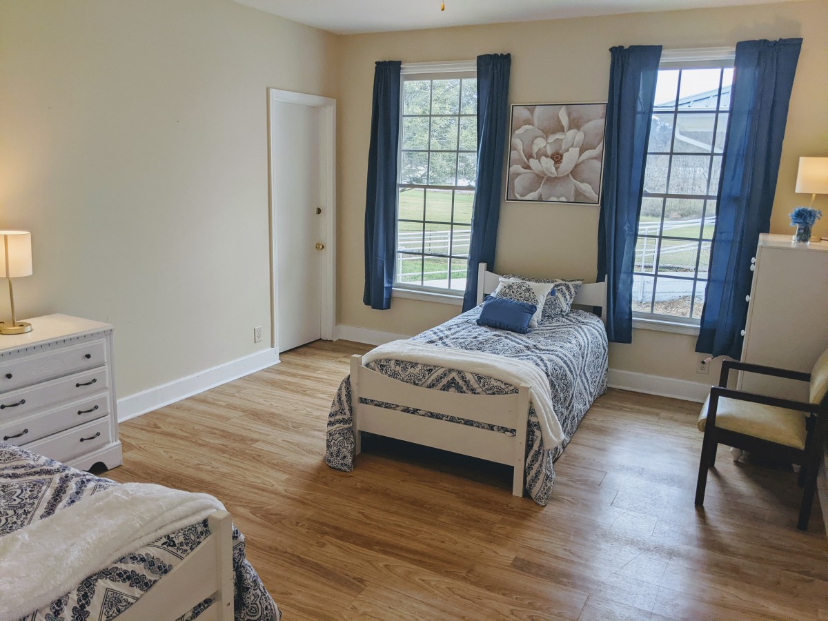 A bright bedroom with twin beds, blue curtains, and wooden flooring.
