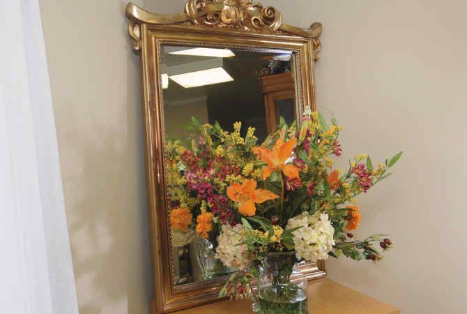 A beautifully arranged bouquet of flowers is reflected in an ornate framed mirror.