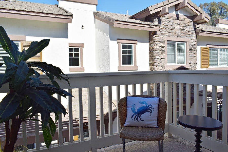 A cozy balcony with a chair featuring a crab-design cushion, overlooking neighboring houses.