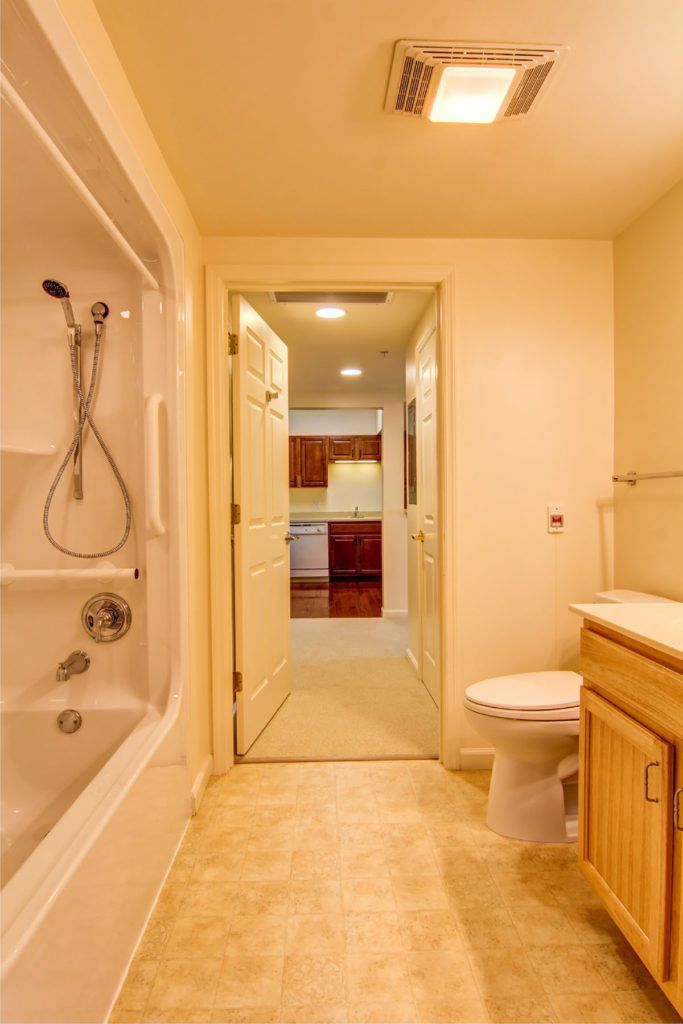 A view of a bathroom interior featuring a bathtub, toilet, and sink with an open doorway leading to another room.