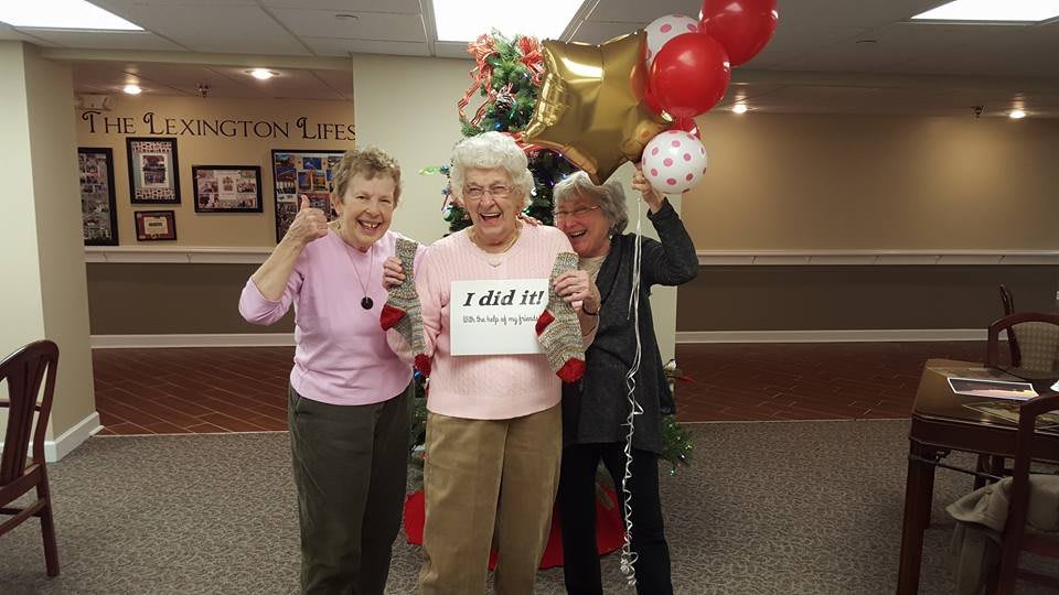 Three senior women celebrating with balloons and a sign.