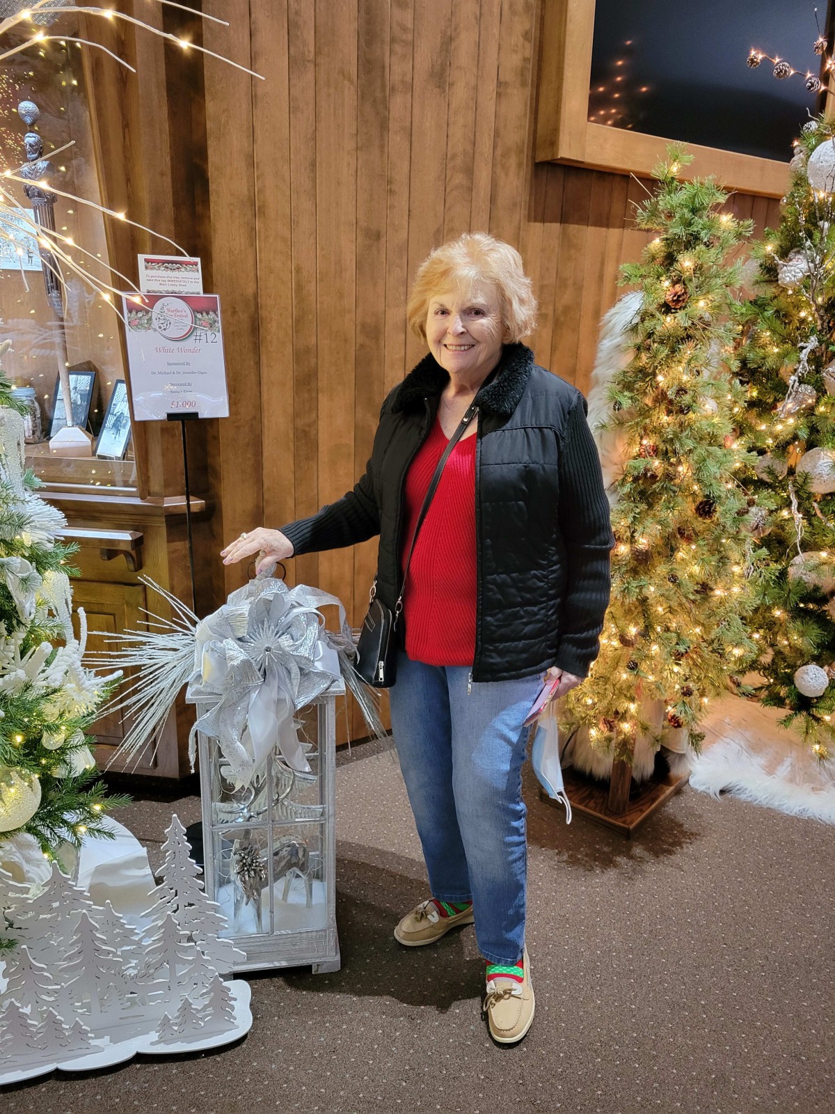 A woman standing next to festive holiday decorations and a Christmas tree.