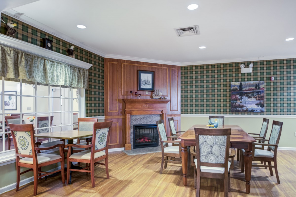 A cozy dining room with elegant wooden furniture and a fireplace, featuring patterned wallpaper and hardwood flooring.
