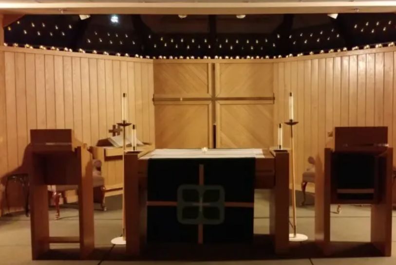 A church altar with wooden paneling, candles, and a prominent cross.