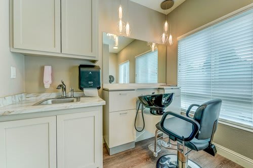 A modern hair salon setup with a styling chair, sink, and well-lit mirror.