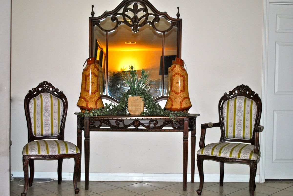 A classic interior setup featuring a carved wooden mirror and matching chairs surrounding a decorative table with ornamental items.