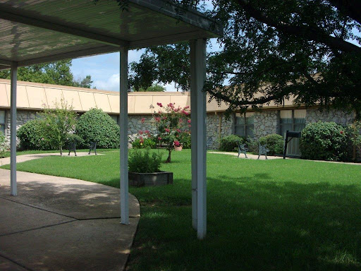 A serene garden area with well-manicured grass and trees, featuring a pathway leading to a building.