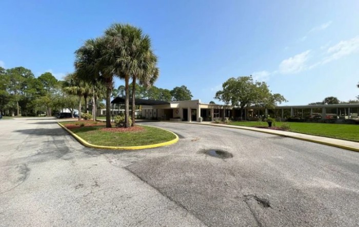 A building with a parking area and palm trees under a clear blue sky.