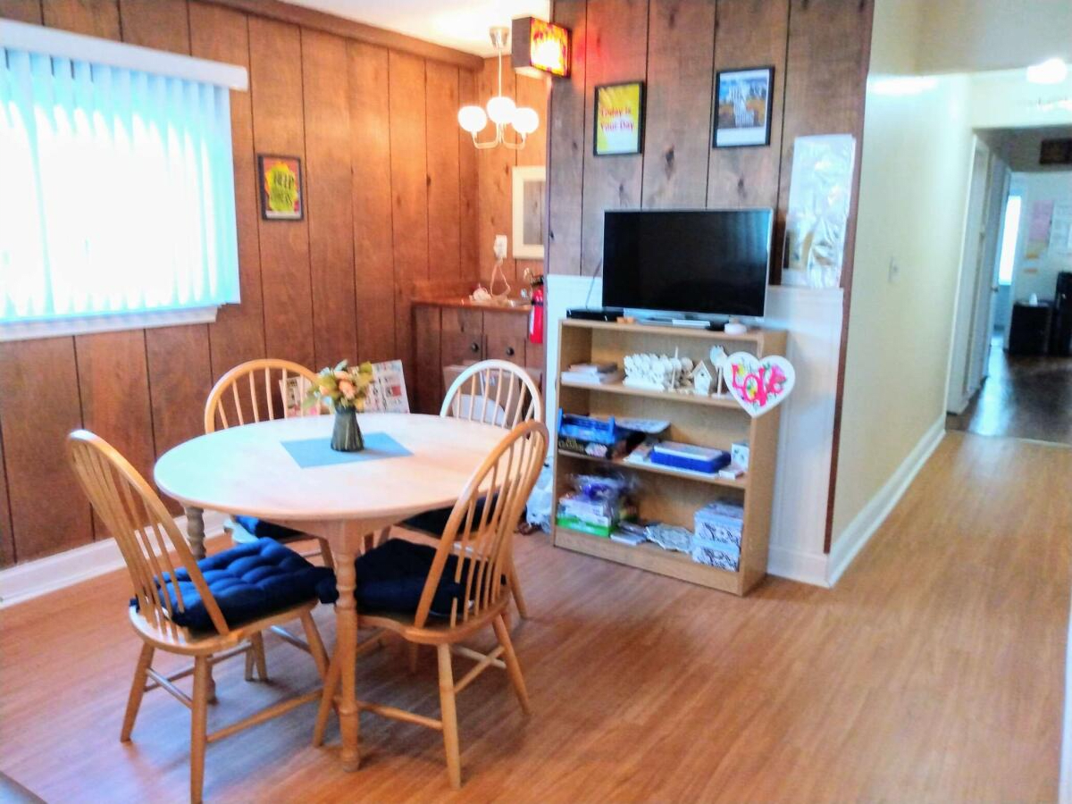 A cozy dining room with wood paneling, featuring a round dining table with chairs and a small entertainment area.