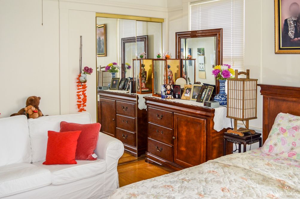 A cozy bedroom featuring a dresser with a mirror, decorative items, and colorful pillows on a white sofa.
