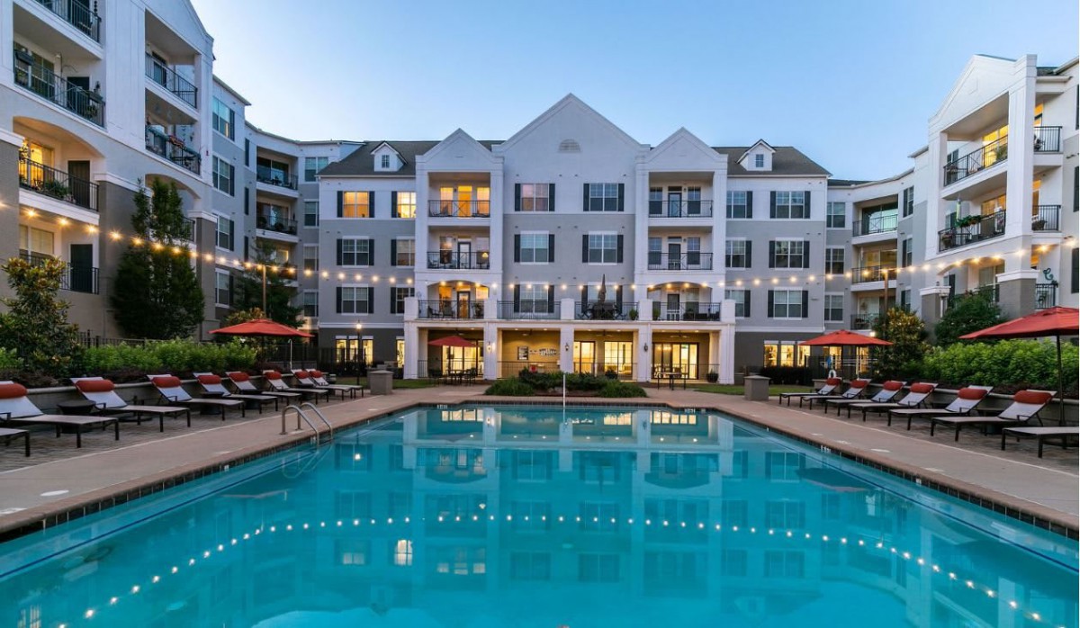 A well-lit apartment complex with a swimming pool at dusk.