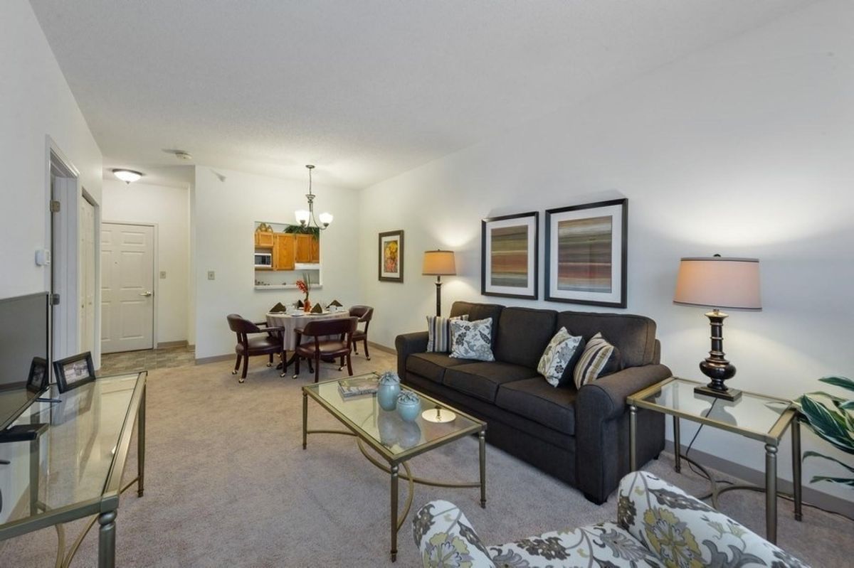 A modern living room with a dining area featuring a sofa, glass coffee table, framed artwork, and decorative lamps.